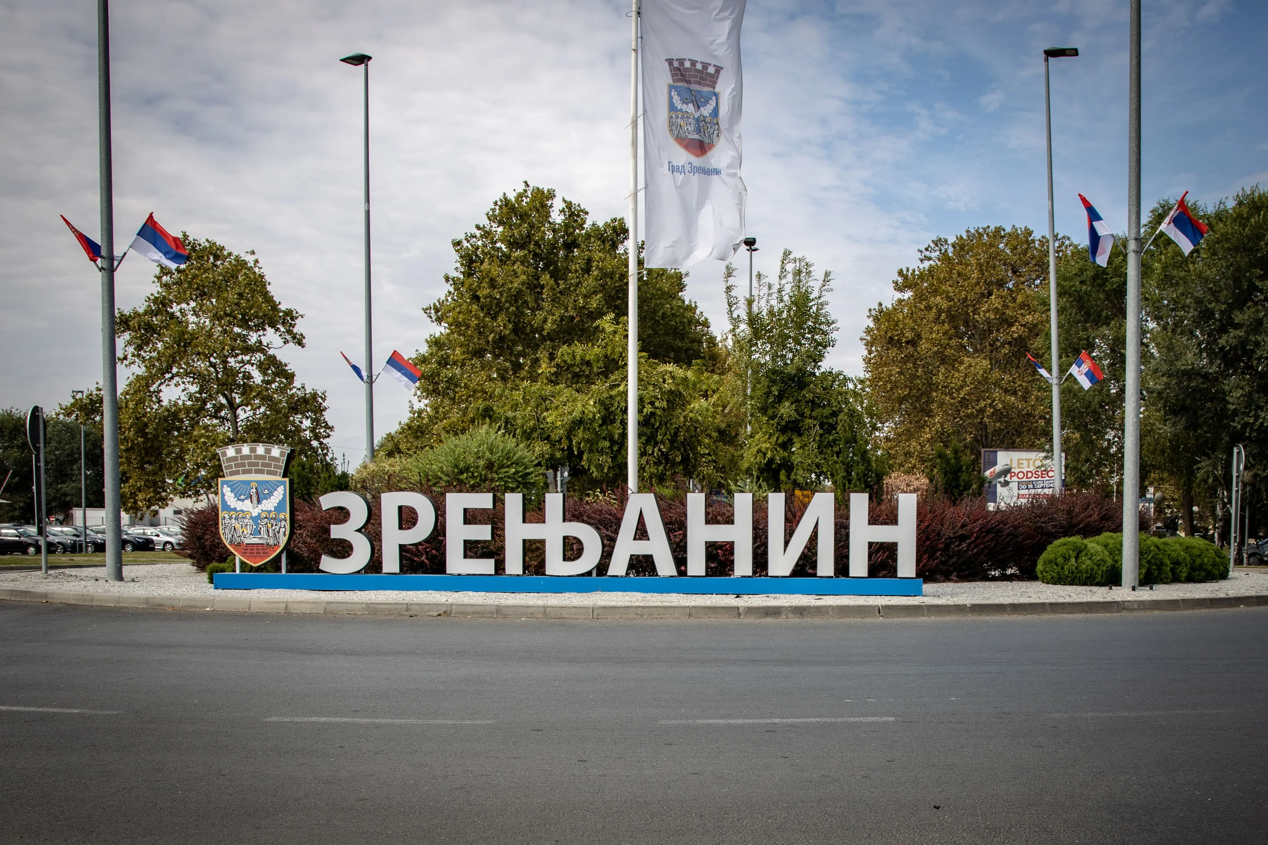 Natpis Zrenjanin sa gradskim grbom, zastavama i drvećem